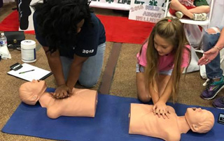LifeNet staff demonstrate compression only CPR with a young girl at Wild About Wellness Health Fair in Texarkana.